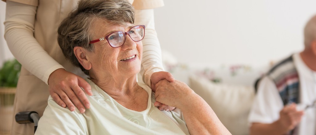 Veduta panoramica di un'anziana signora in sedia a rotelle che tiene per mano un volontario in piedi alle sue spalle
