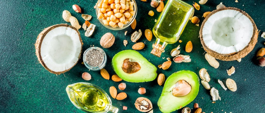 vari alimenti che contengono omega-3, quali avocado olio di oliva e mandorle, sparpagliati su un tavolo