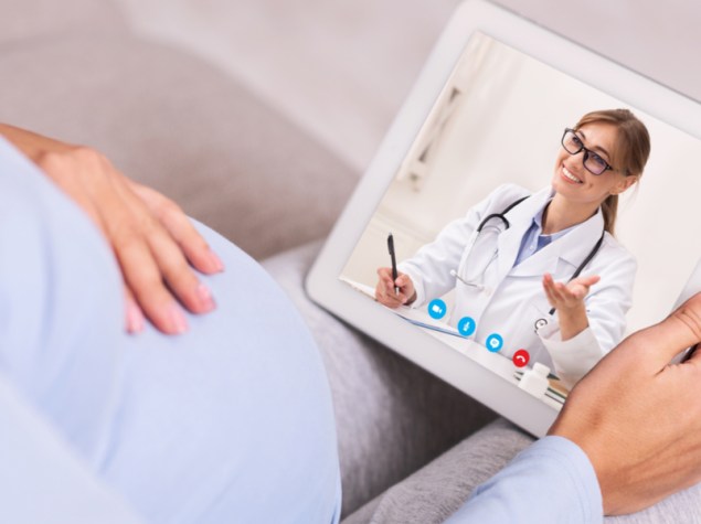 donna incinta seduta sul divano che effettua una chiamata al suo dottore tramite tablet