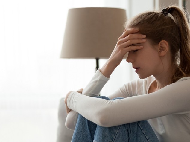 giovane donna seduta sul divano con la mano sulla fronte, in stato di ansia