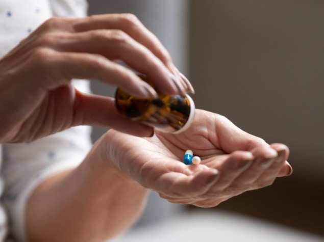 donna che estrae due pillole di farmaci da un flacone trasparente