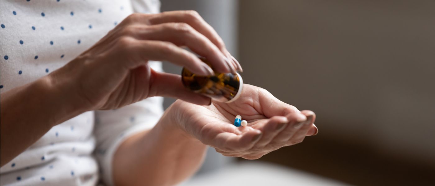 donna che estrae due pillole di farmaci da un flacone trasparente