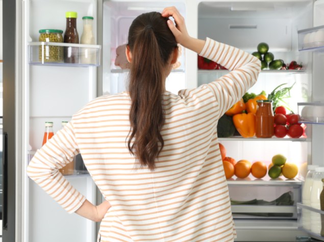 donna che guarda nel frigo dubbiosa su quali alimenti mangiare