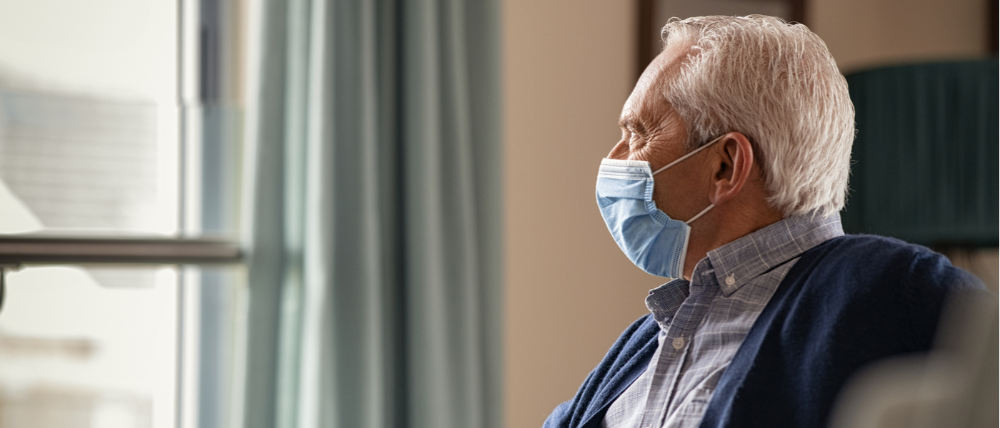 anziano con mascherina che guarda fuori da finestra
