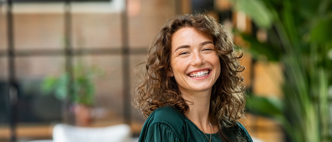 Ritratto di giovane donna sorridente che guarda la fotocamera con le braccia incrociate. Ragazza felice in piedi in un ufficio creativo. Donna d'affari di successo in piedi in ufficio con spazio per le copie.