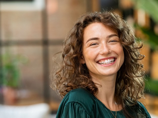 Ritratto di giovane donna sorridente che guarda la fotocamera con le braccia incrociate. Ragazza felice in piedi in un ufficio creativo. Donna d'affari di successo in piedi in ufficio con spazio per le copie.