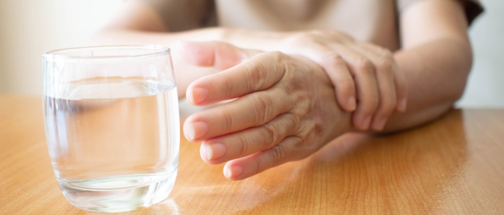 Una donna con la mano che trema prova a prendere un bicchiere d'acqua