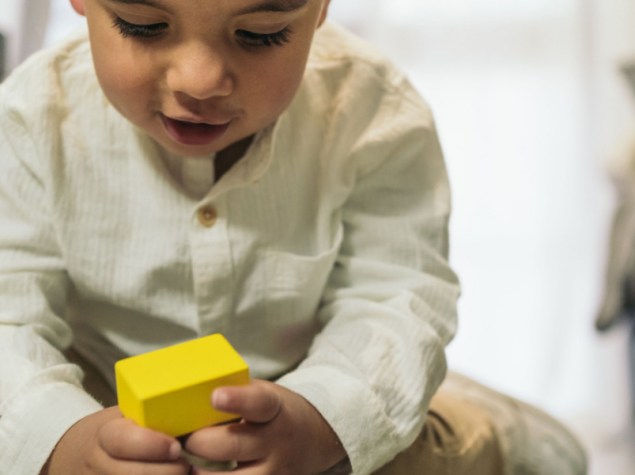 Frontal image of a young autistic child playing at stacking colorful wooden pieces on the living room floor.