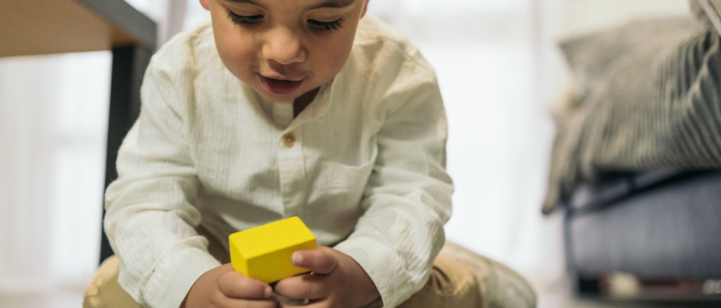 Frontal image of a young autistic child playing at stacking colorful wooden pieces on the living room floor.