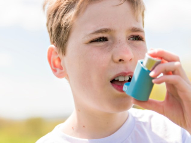 bambino che usa l'inalatore per l'asma all'aperto in un parco