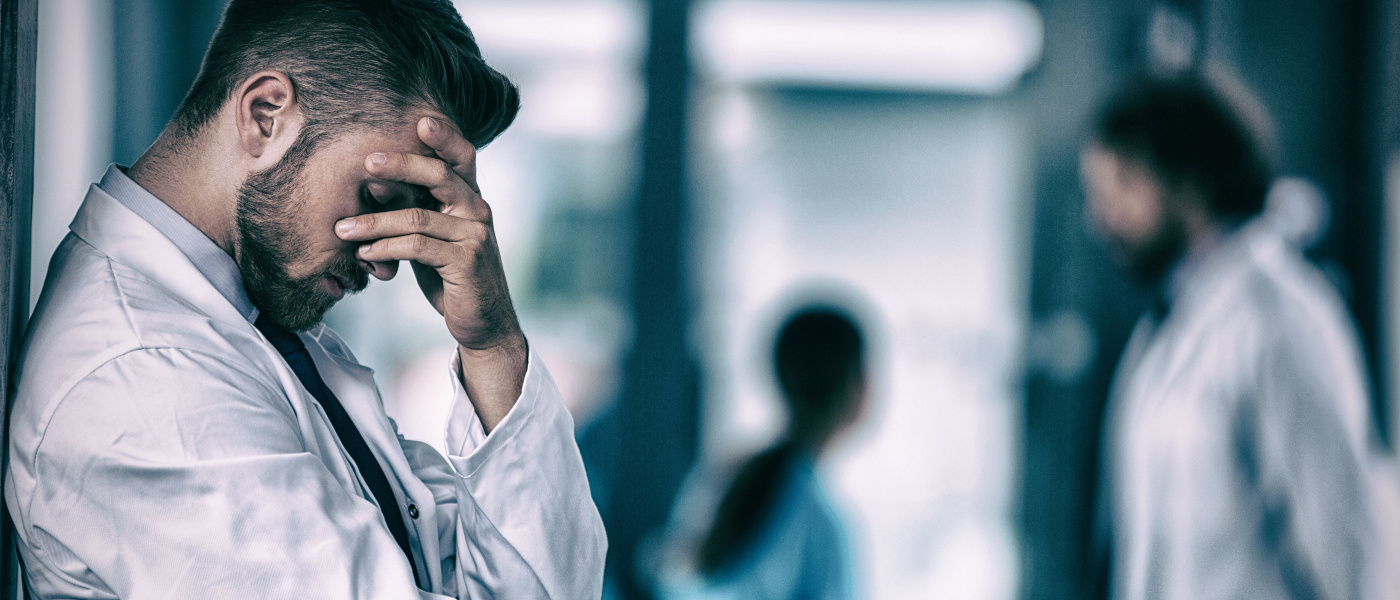 giovane medico stressato appoggiato muro mano sul viso