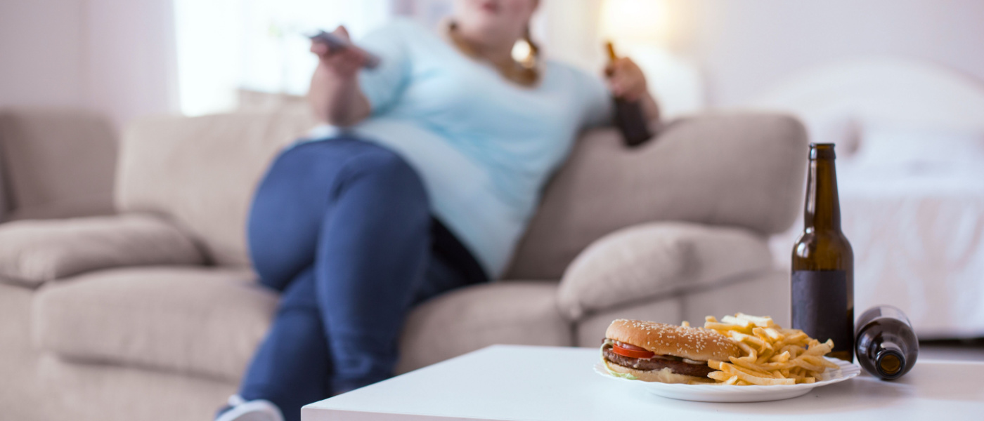 ragazza obesa seduta sul divano guarda televisione e mangia cibi grassi