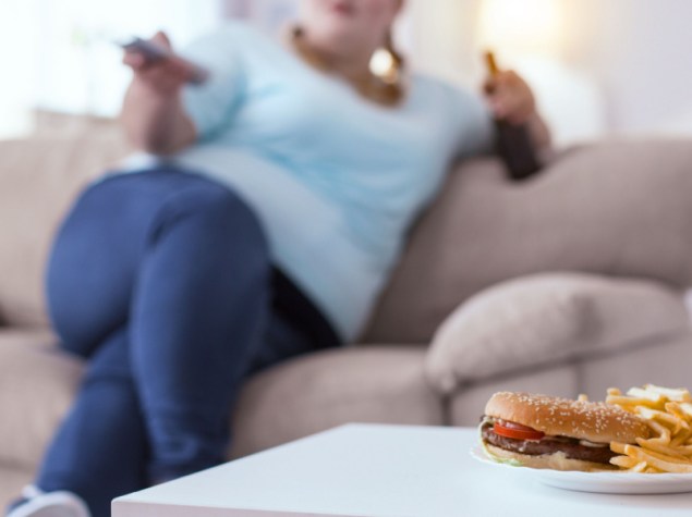 ragazza obesa seduta sul divano guarda televisione e mangia cibi grassi