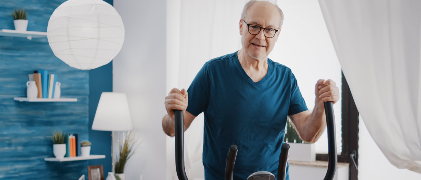 Anziano adulto che fa esercizio fisico cardio sulla bicicletta da fitness. Uomo anziano che utilizza una cyclette elettrica per allenarsi a casa. Anziano con attrezzatura sportiva per tenersi in forma.