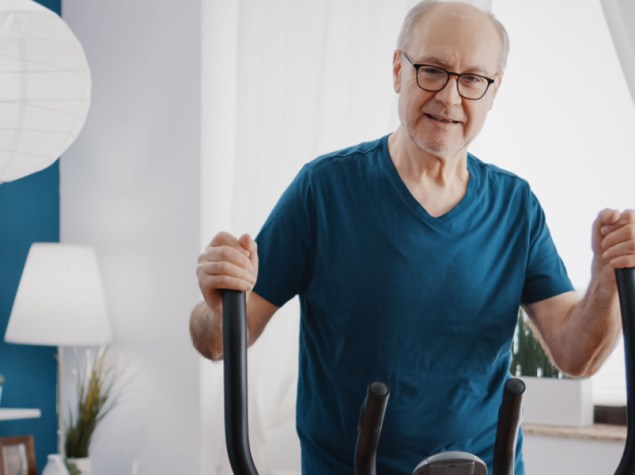 Anziano adulto che fa esercizio fisico cardio sulla bicicletta da fitness. Uomo anziano che utilizza una cyclette elettrica per allenarsi a casa. Anziano con attrezzatura sportiva per tenersi in forma.