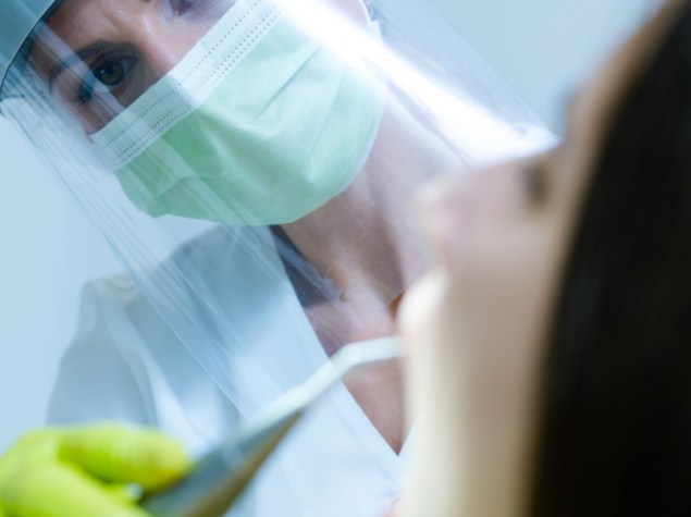 Una dentista che indossa maschera, guanti e visiera come precauzione di sicurezza per il coronavirus controlla la salute dentale di una giovane donna