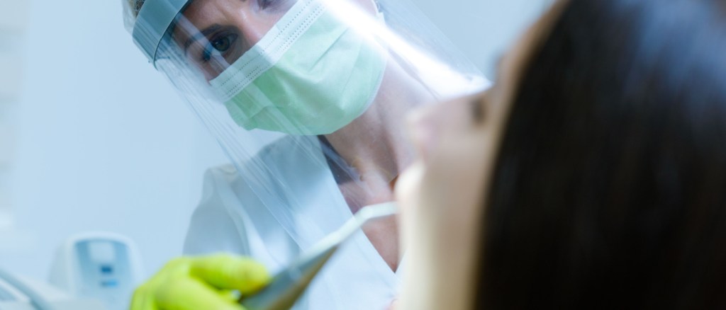 Una dentista che indossa maschera, guanti e visiera come precauzione di sicurezza per il coronavirus controlla la salute dentale di una giovane donna