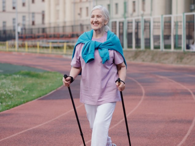 Donna anziana pratica nordic walk. Anziana signora scandinava pole hike stadio. Nonna sport allenamento Europa. Stile di vita delle donne in salute.