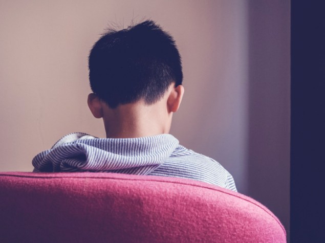 bambino triste seduto di spalle su una poltrona