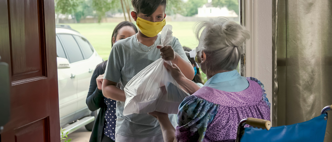 Dando il buon esempio, questa madre, che fa parte di un programma di volontariato per la consegna di cibo, porta con sé i figli per consegnare il cibo a un'anziana in sedia a rotelle.