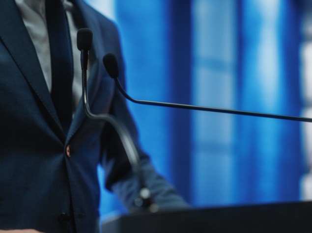 uomo in giacca e cravatta che parla da un palco