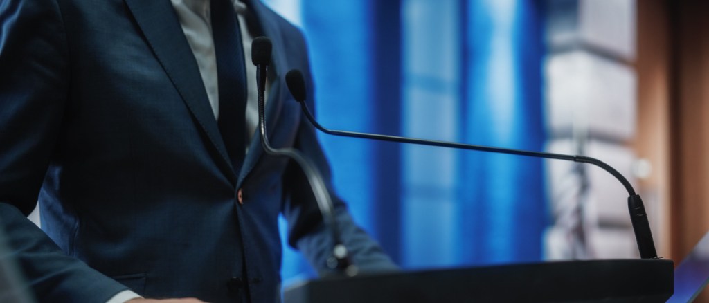 uomo in giacca e cravatta che parla da un palco