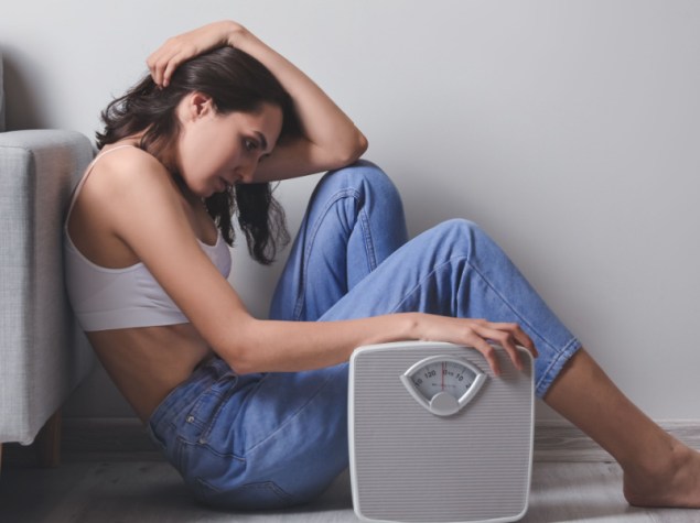 ragazza magra e triste seduta per terra con una bilancia in mano