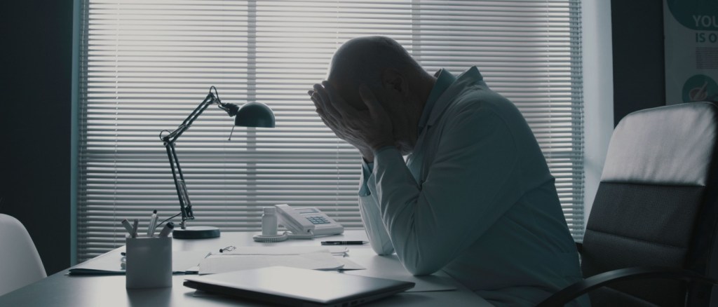 Lavoratore con mani sul viso ad una scrivania