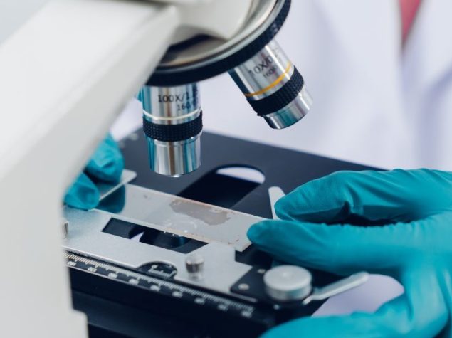 Uno scienziato esamina i campioni con un microscopio in un laboratorio con provette riempite di liquido colorato