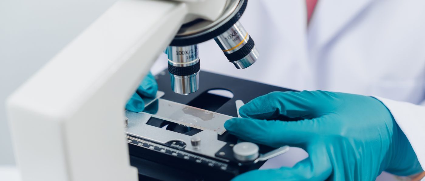 Uno scienziato esamina i campioni con un microscopio in un laboratorio con provette riempite di liquido colorato