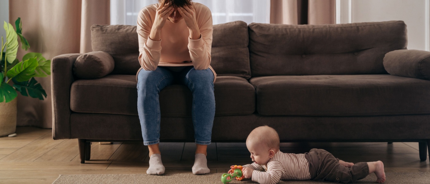 Mamma seduta sul divano in stato di depressione con bambino che gioca sul pavimento