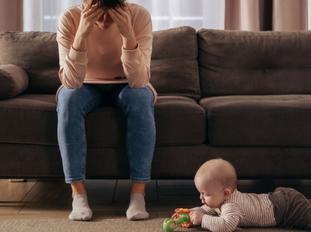 Mamma seduta sul divano in stato di depressione con bambino che gioca sul pavimento