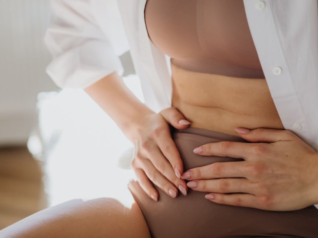 Giovane donna si tocca con le mani basso addome per dolore