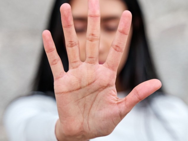donna con il braccio disteso e la mano che le copre il viso, con un gesto per dire "basta". Campagna per fermare la violenza contro le donne
