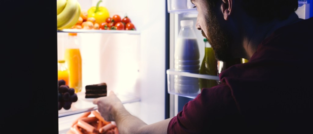 Uomo prende cibo dal frigorifero di notte