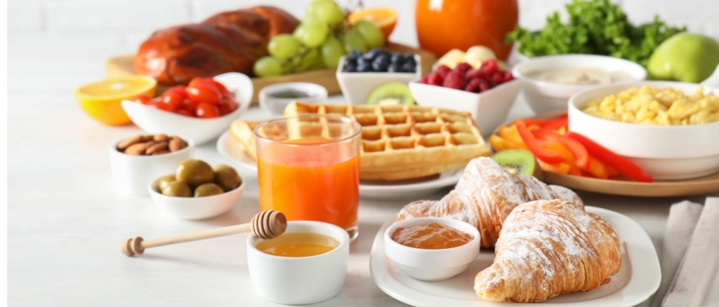 Tavolo imbandito per colazione con cornetti, frutta fresca e bevande