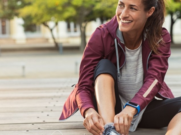 Donna seduta a terra in tenuta sportiva che si allaccia una scarpa