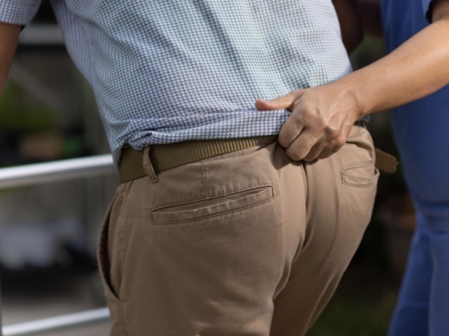 Infermiere che tiene dalla cintura un paziente con deambulatore per aiutarlo a stare in piedi e camminare