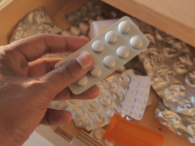 Mano con confezione di pillole sopra un cassetto dei medicinali in disordine