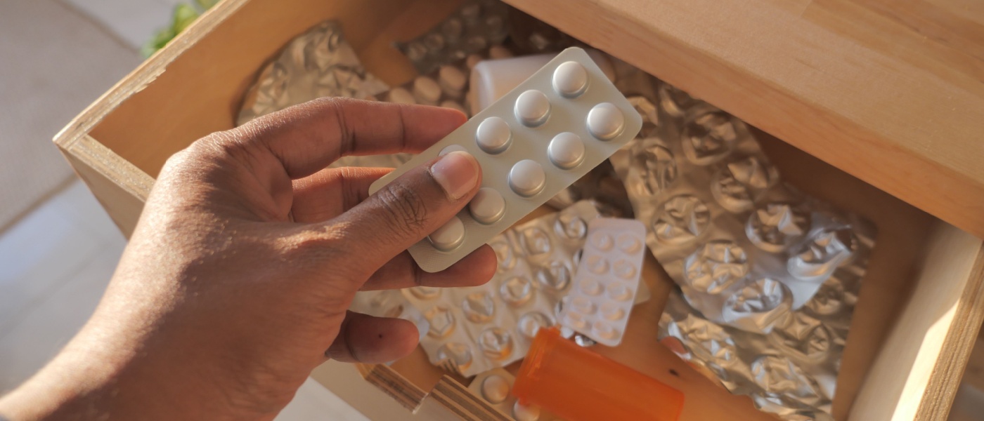 Mano con confezione di pillole sopra un cassetto dei medicinali in disordine