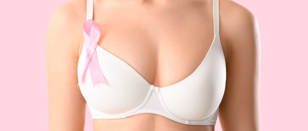 Giovane donna in reggiseno e con nastro di sensibilizzazione su sfondo rosa