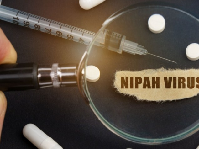 Un uomo guarda attraverso una lente d'ingrandimento delle pillole, una siringa e un pezzo di carta con la scritta virus Nipah