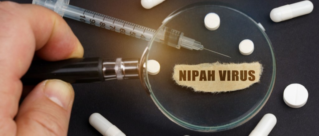 Un uomo guarda attraverso una lente d'ingrandimento delle pillole, una siringa e un pezzo di carta con la scritta virus Nipah