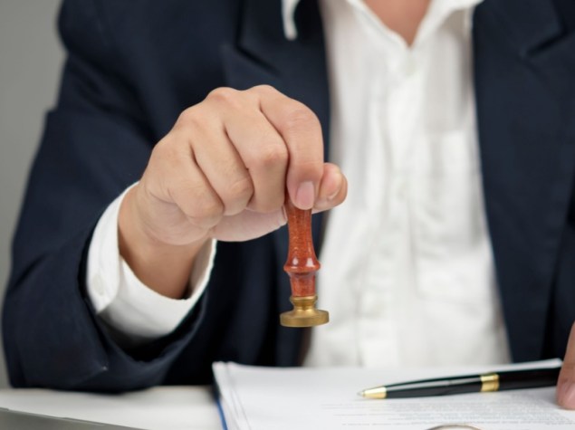 Mano del manager con un timbro per l'approvazione finale del documento aziendale