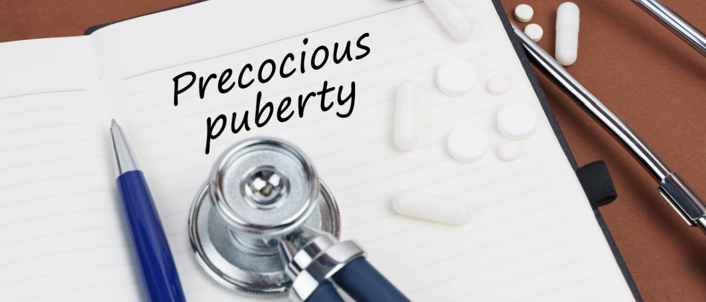 pillole, una penna, uno stetoscopio e un quaderno con la scritta "Pubertà precoce"