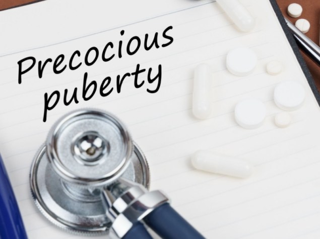 pillole, una penna, uno stetoscopio e un quaderno con la scritta "Pubertà precoce"