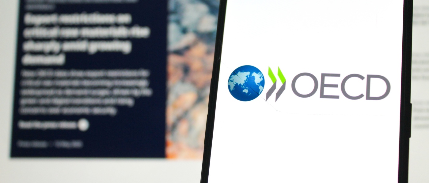 Logo dell'OCSE visualizzato su un telefono cellulare con il sito web ufficiale dell'OCSE sullo sfondo