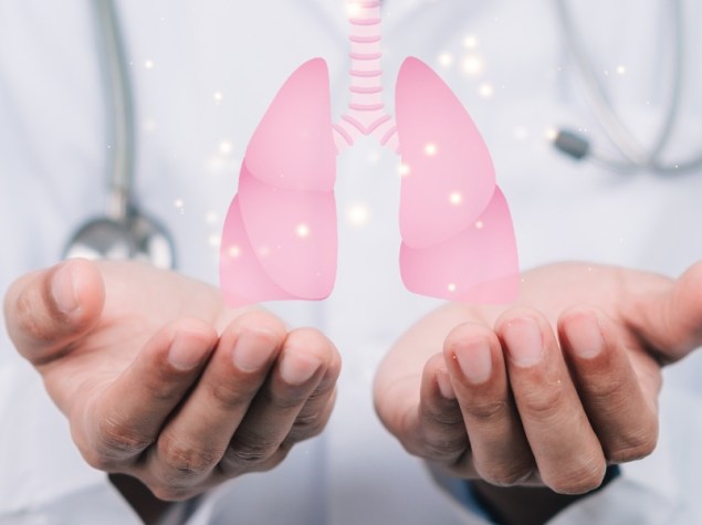 Un medico in camice tiene in mano un simbolo a forma di polmone mentre è seduto a un tavolo in ospedale