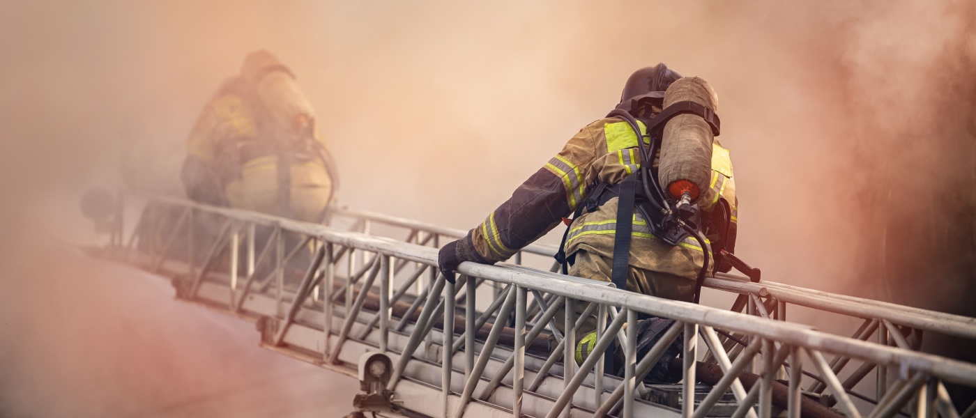 vigili del fuoco si arrampicano su una scala all'interno di una casa in fiamme, attraversando il fumo