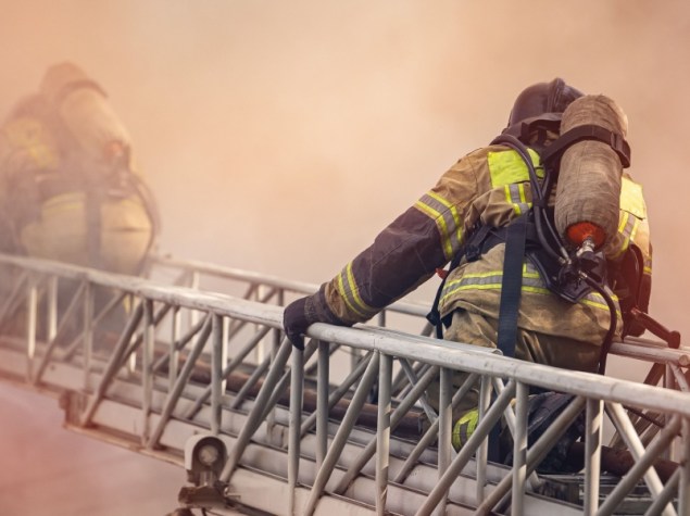 vigili del fuoco si arrampicano su una scala all'interno di una casa in fiamme, attraversando il fumo